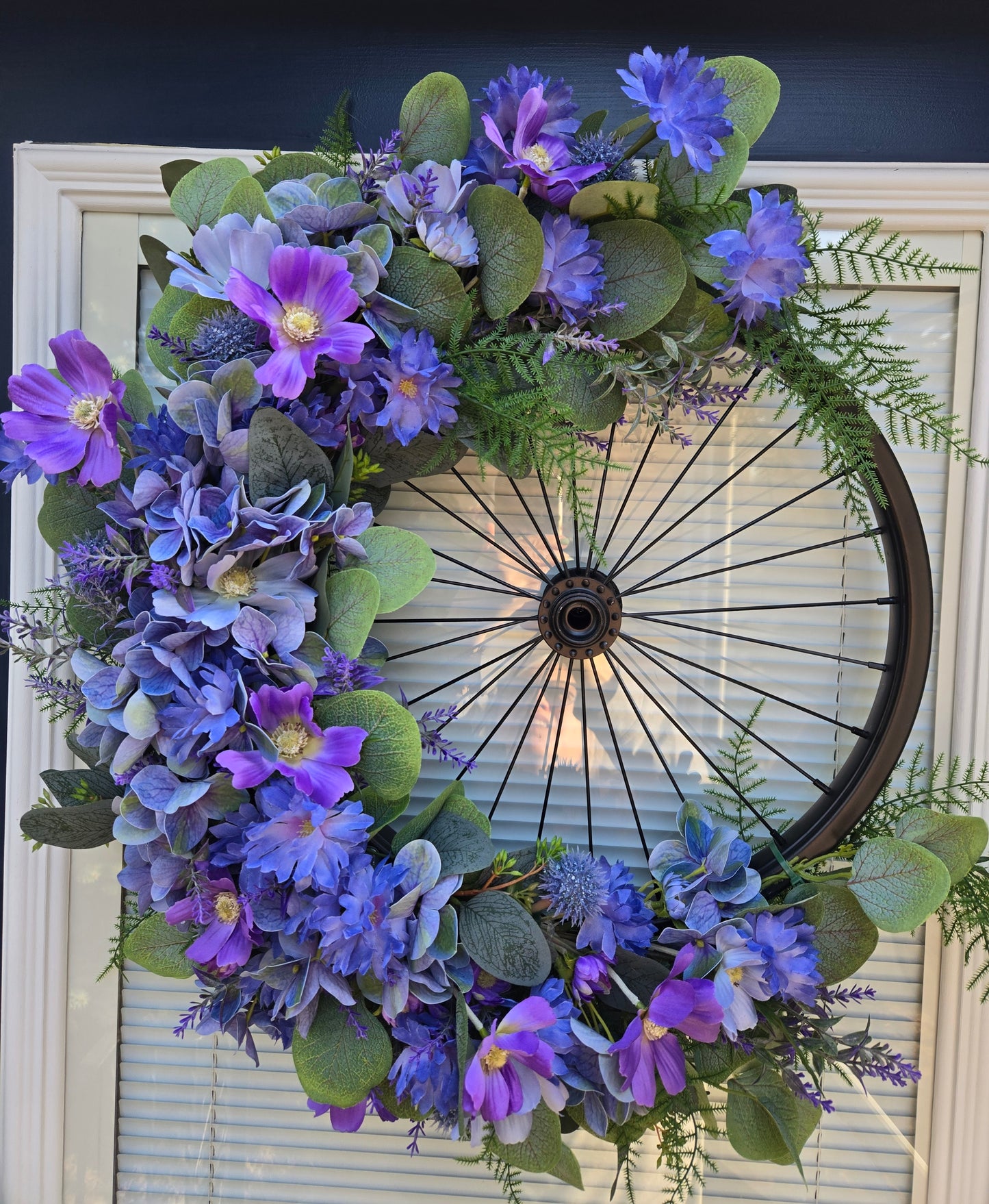 Bicycle Rim Wreath black with artificial flowers in blues and purple.