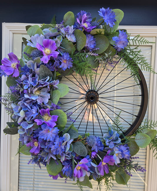 Bicycle Rim Wreath black with artificial flowers in blues and purple.